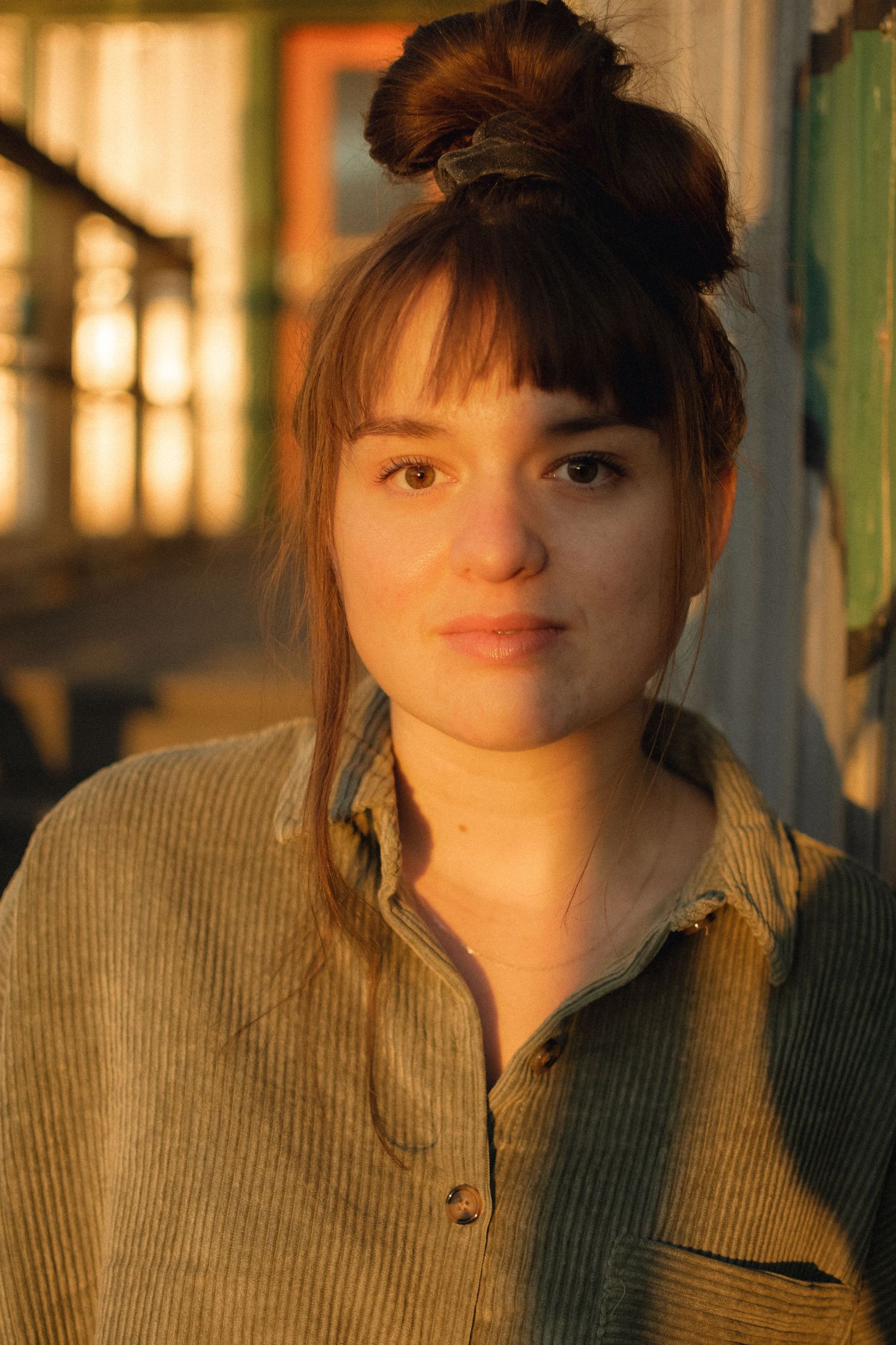 A warm-toned portrait featuring a corduroy shirt and hair in a bun during sunset lighting.