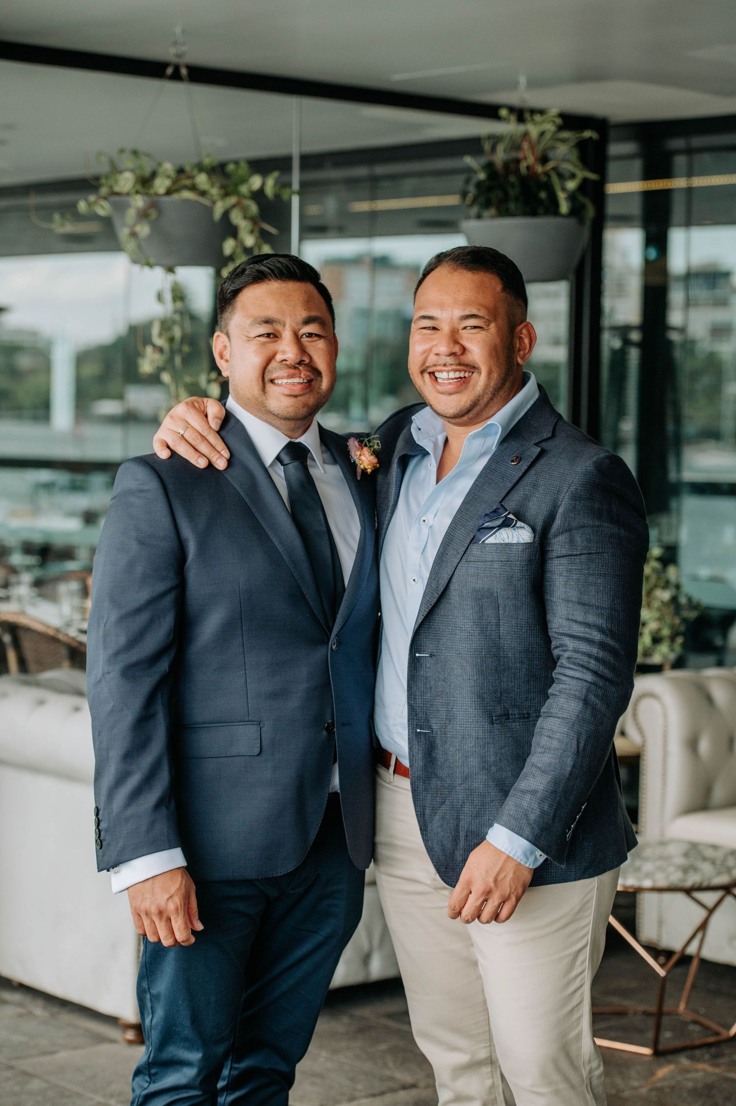 Two men in formal attire smile warmly at a wedding celebration.