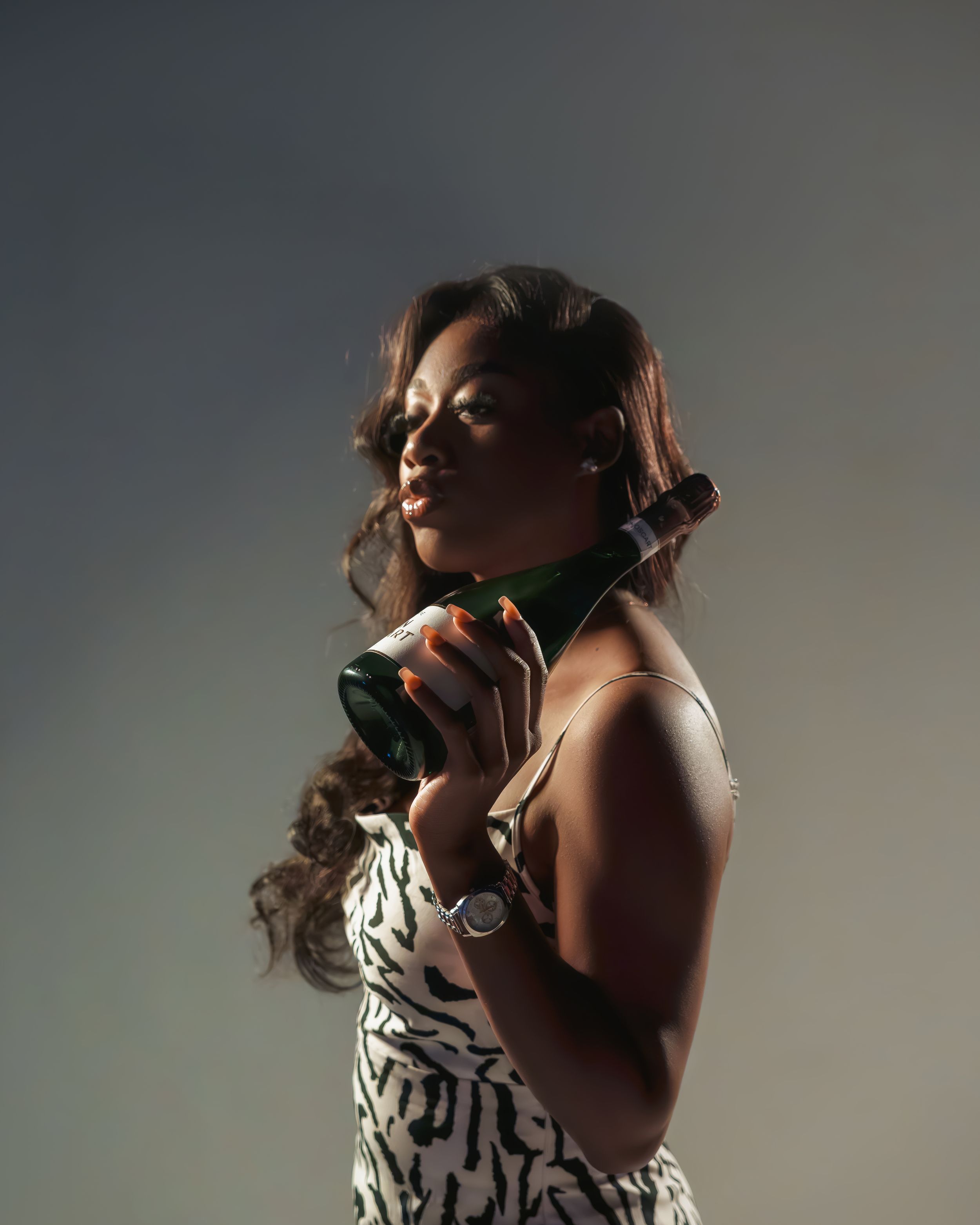 Stylish woman in patterned dress holding champagne glass in dramatic lighting against dark background.