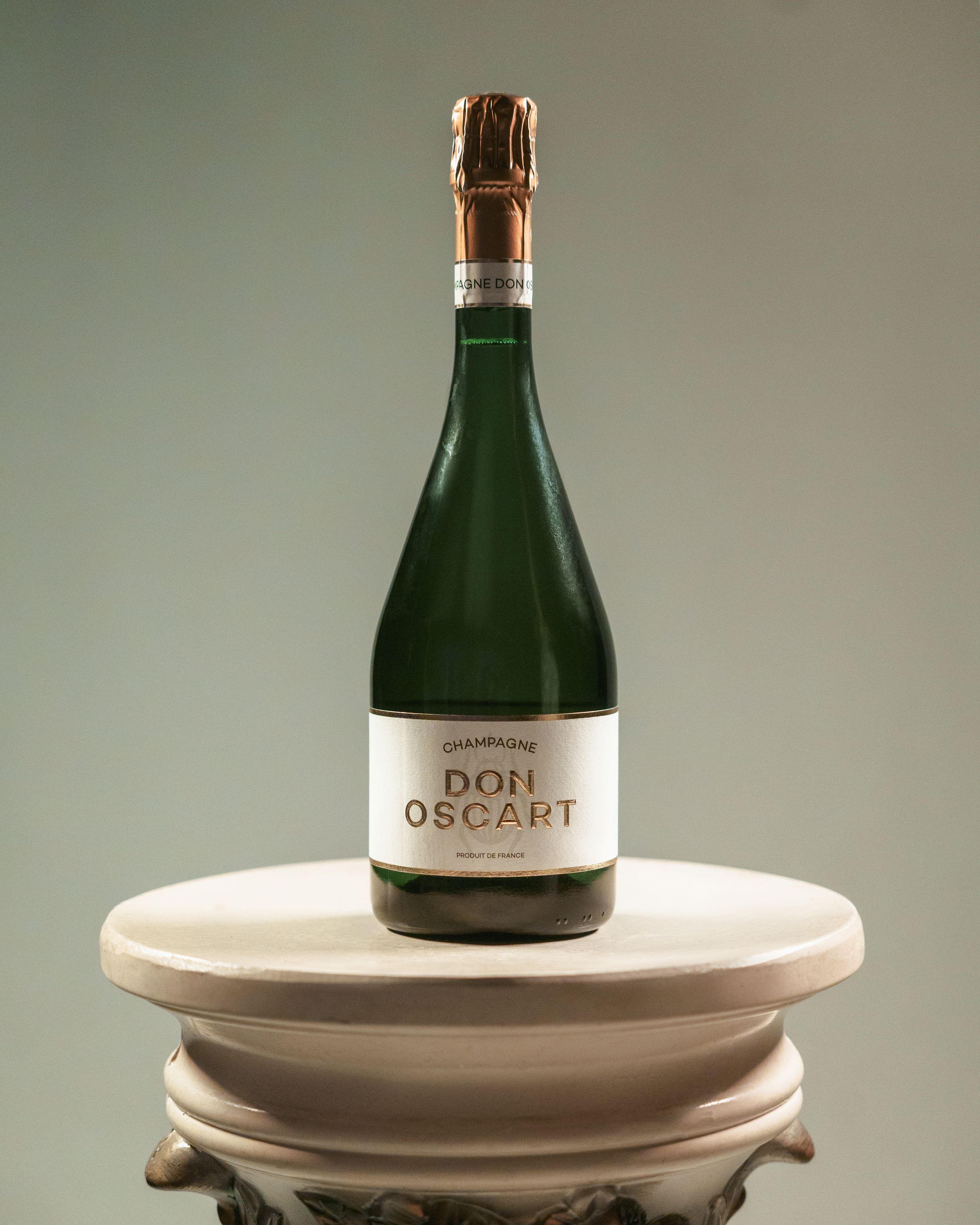 Bottle of Don Oscar champagne displayed on decorative white pedestal.