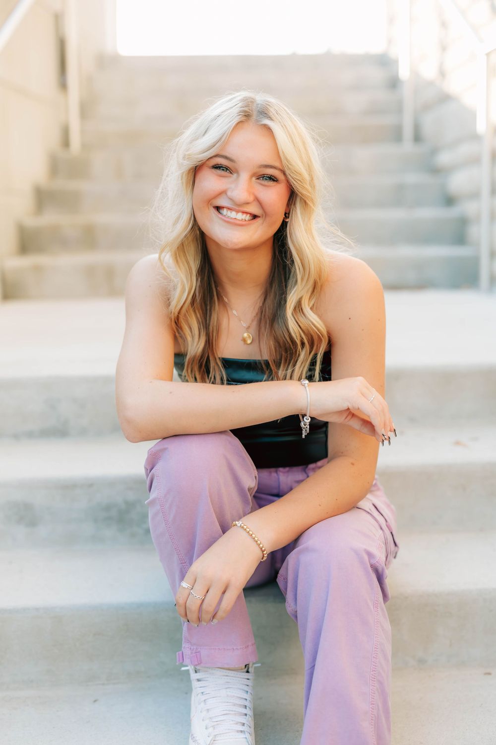Portrait of someone sitting on concrete steps wearing purple pants and white sneakers.