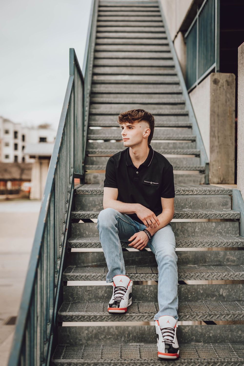 Casual portrait on concrete steps wearing black polo and light denim.
