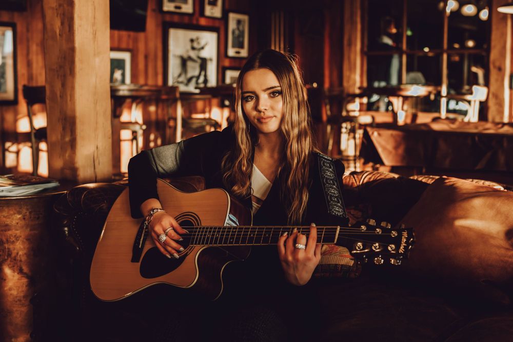 Woman plays acoustic guitar in warmly lit rustic bar setting.