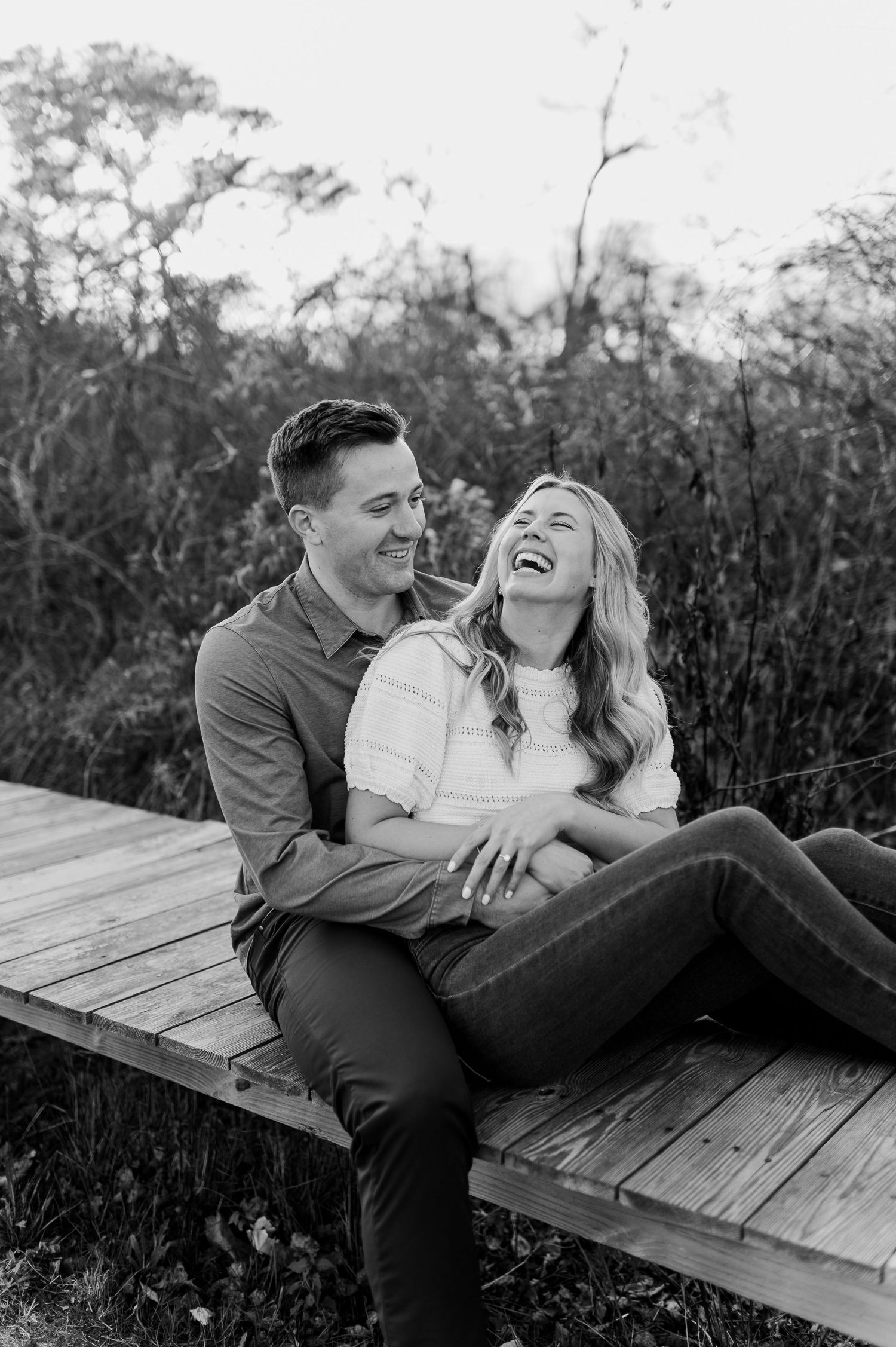 Couple sharing joyful laughter while relaxing on wooden bench in black and white photography.