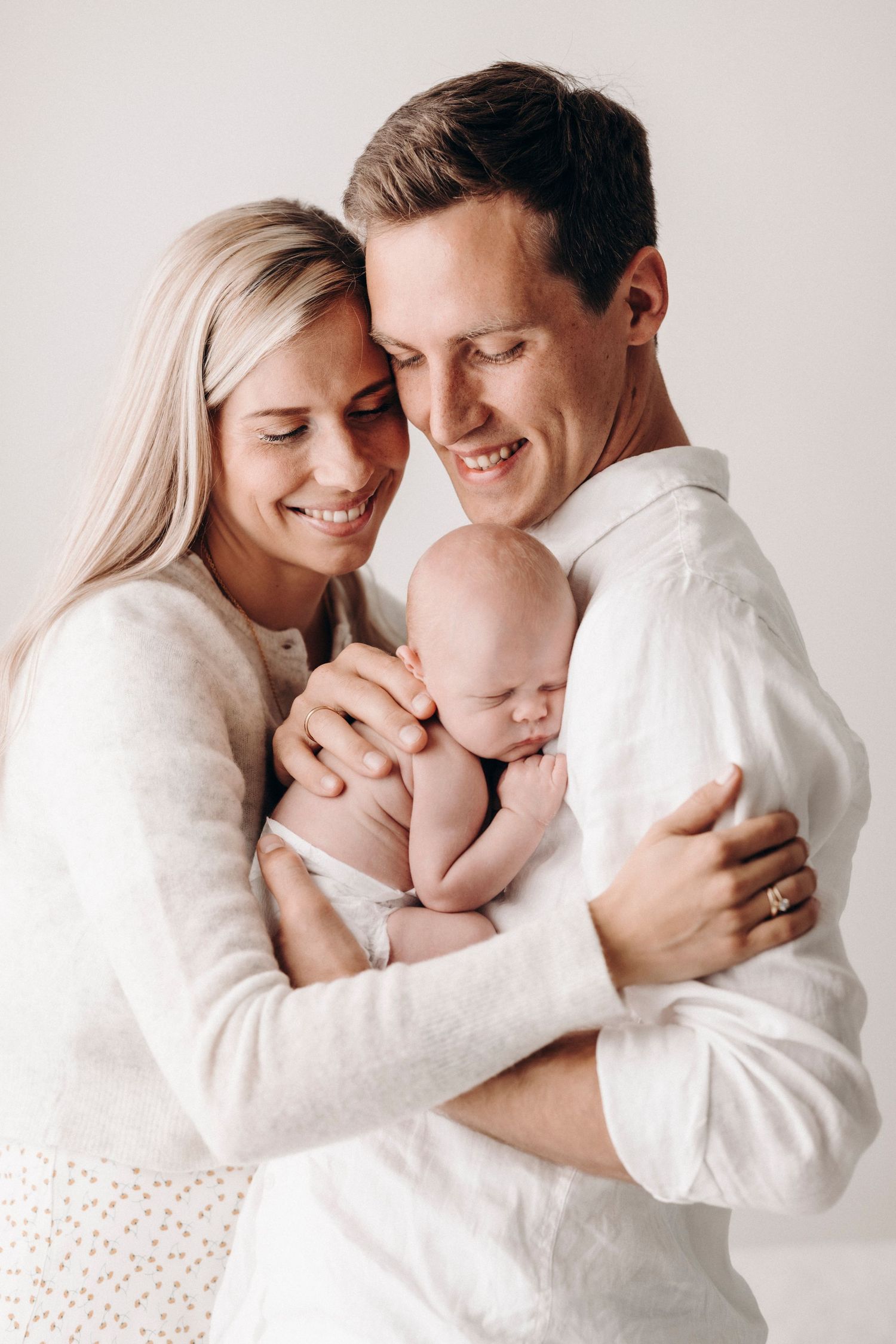 Intimate family portrait showing loving embrace with newborn baby against white background.
