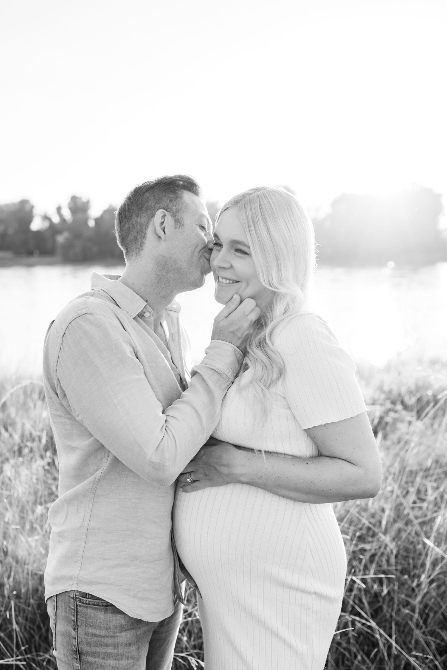 Intimate maternity portrait captured in soft sunlight by the water.