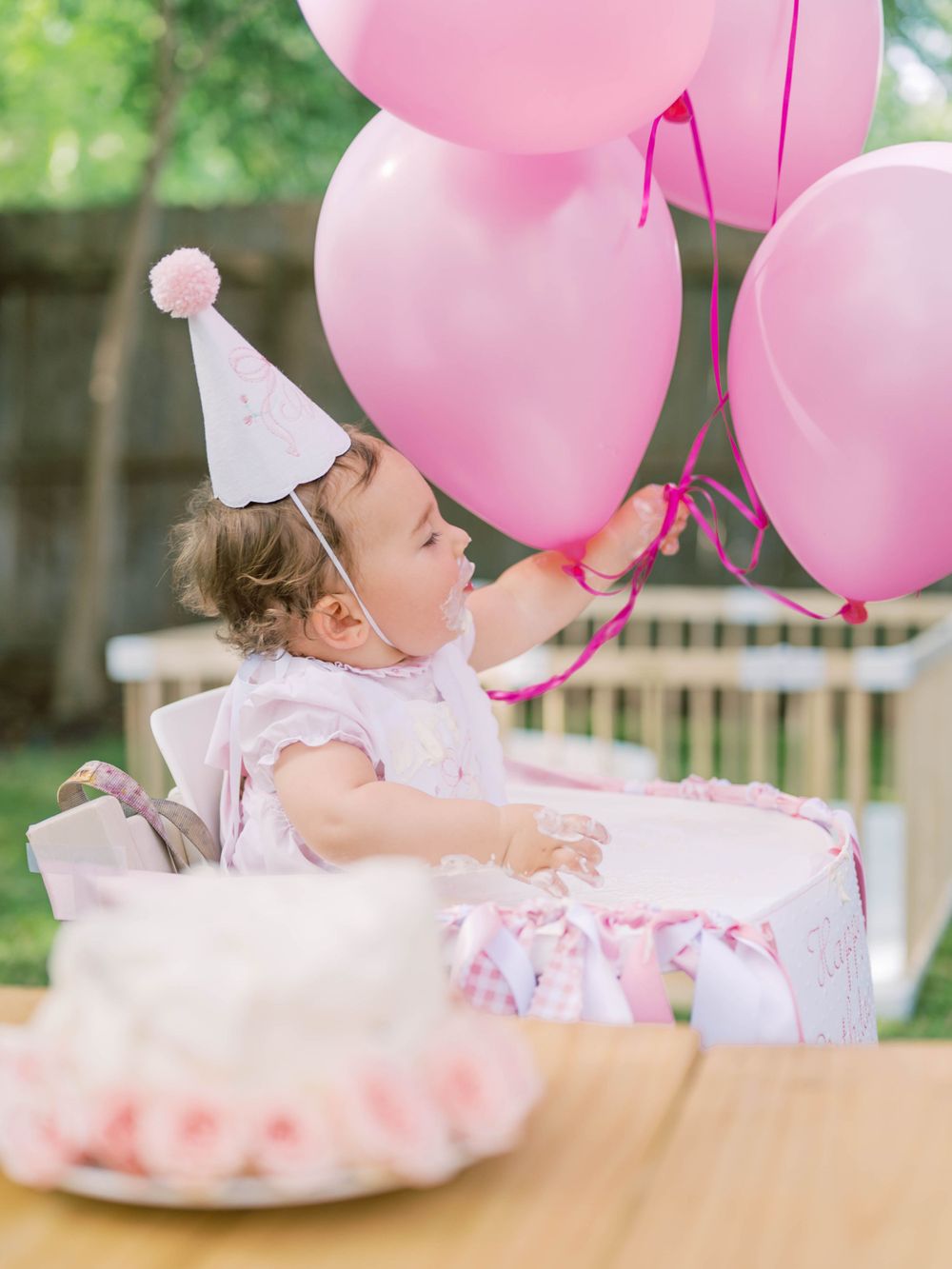 photo of a little girl holding pink balloons with a cake at her first birthday party