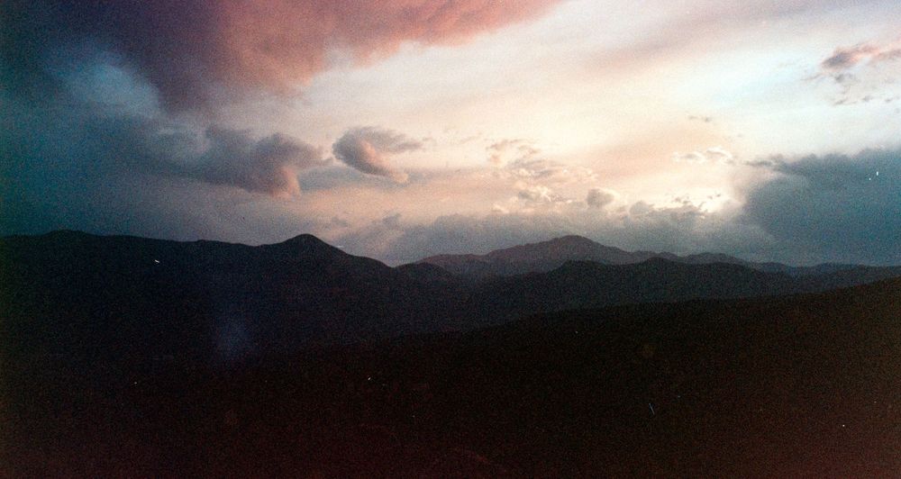 Dramatic sunset over dark mountain silhouettes with moody clouds in the sky.