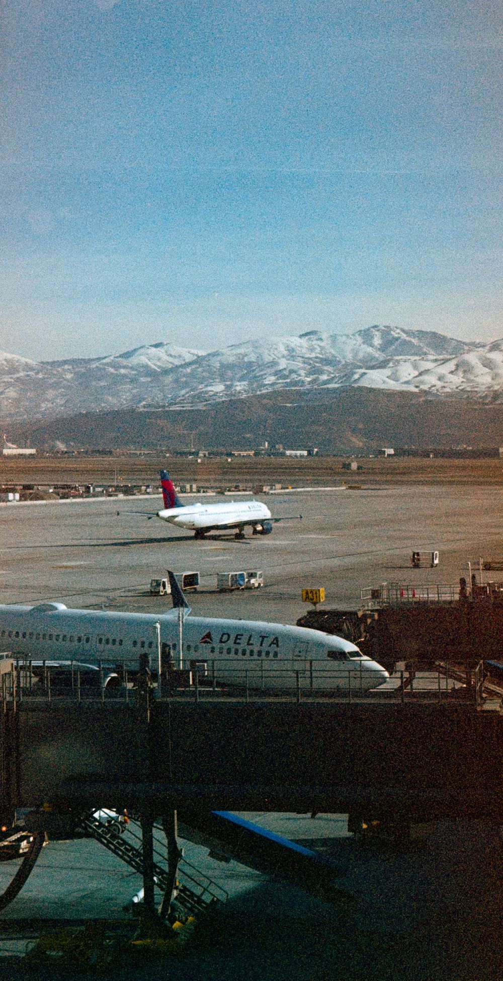 Delta airplanes parked at mountain airport with snow-capped peaks in background.
