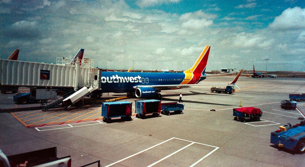 Southwest Airlines plane parked at airport terminal with luggage carts on tarmac.