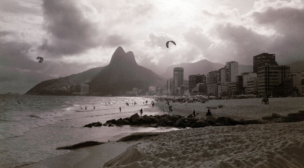 Dramatic sky over Ipanema Beach with mountain peaks and high-rise buildings along the coast.