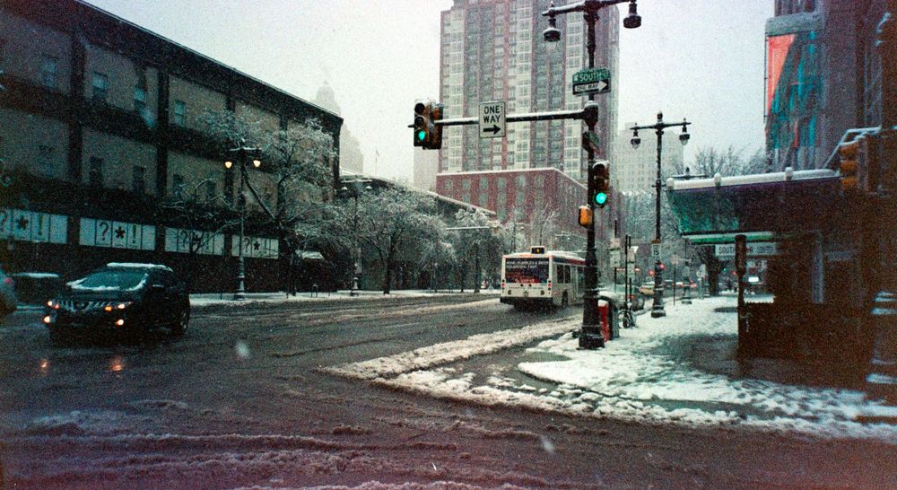 Snowy urban street corner with traffic lights and tall buildings in winter.