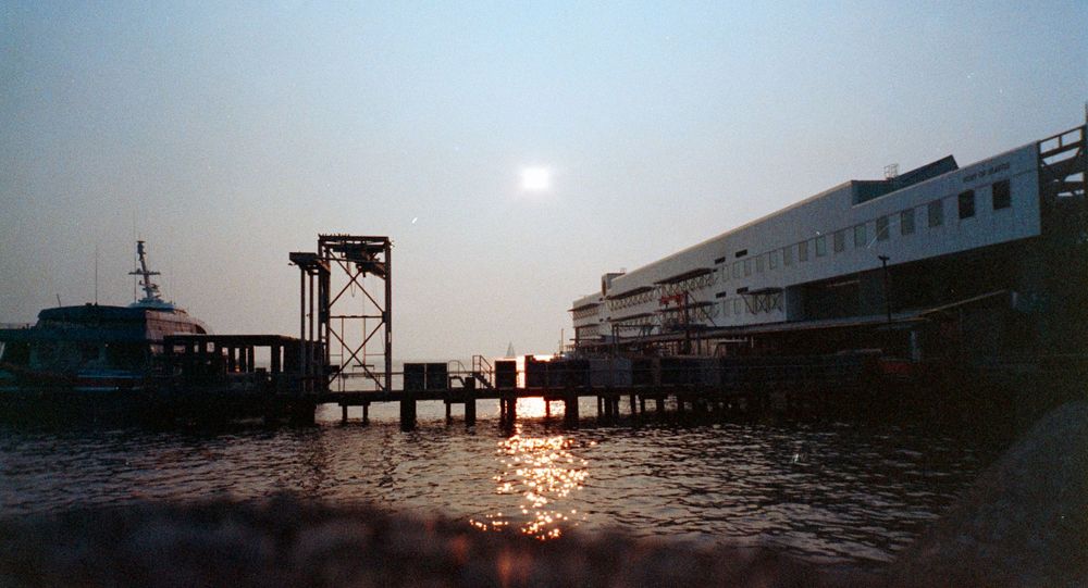 Industrial waterfront dock and building silhouetted against a hazy sunset sky.