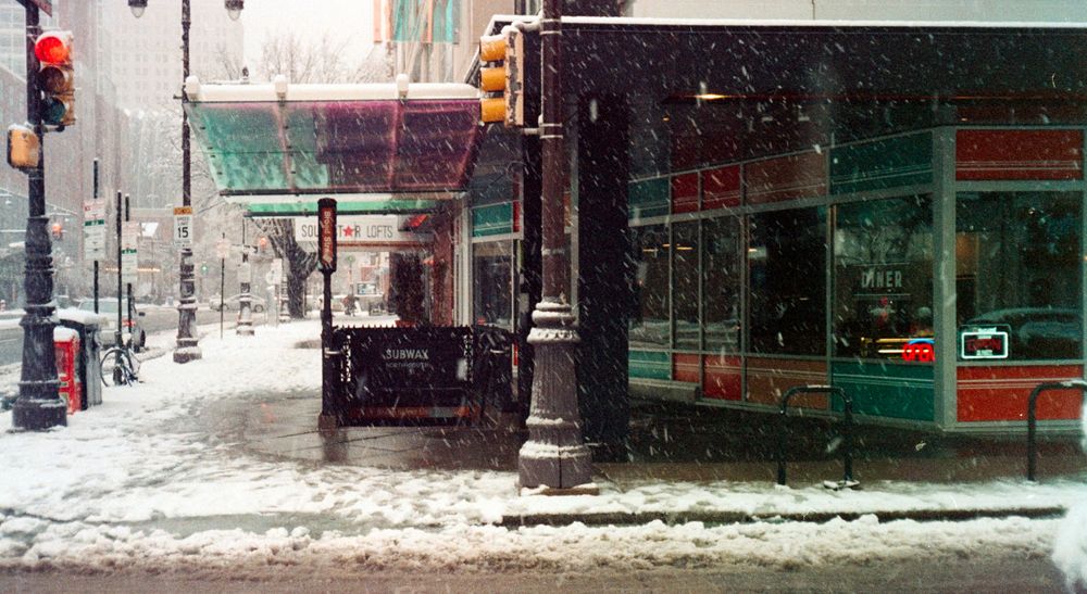 Snow covered storefront with traffic light and street signs in an urban setting.