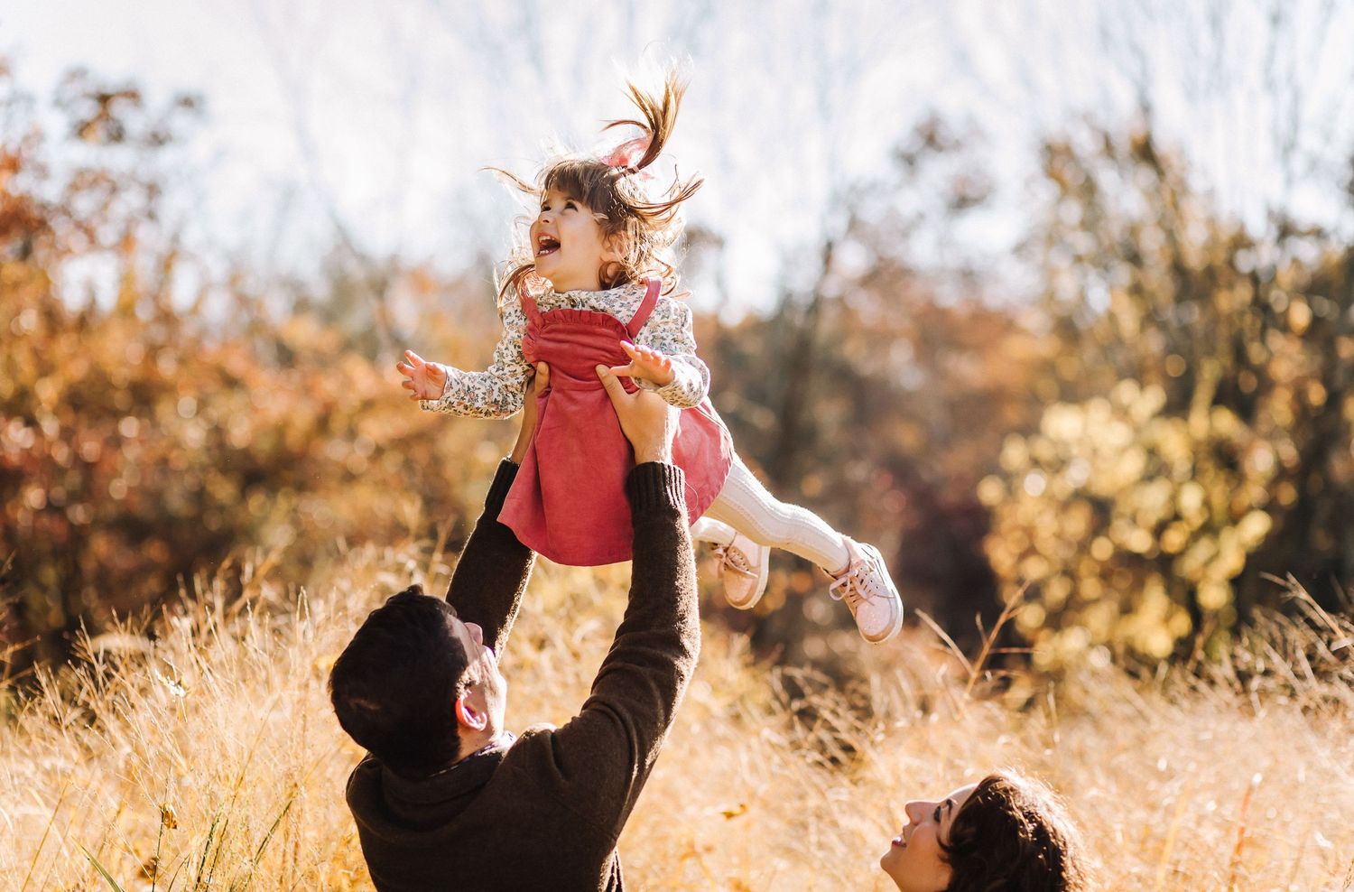 A joyful moment captured in golden sunlight as a child is lifted high into the air.
