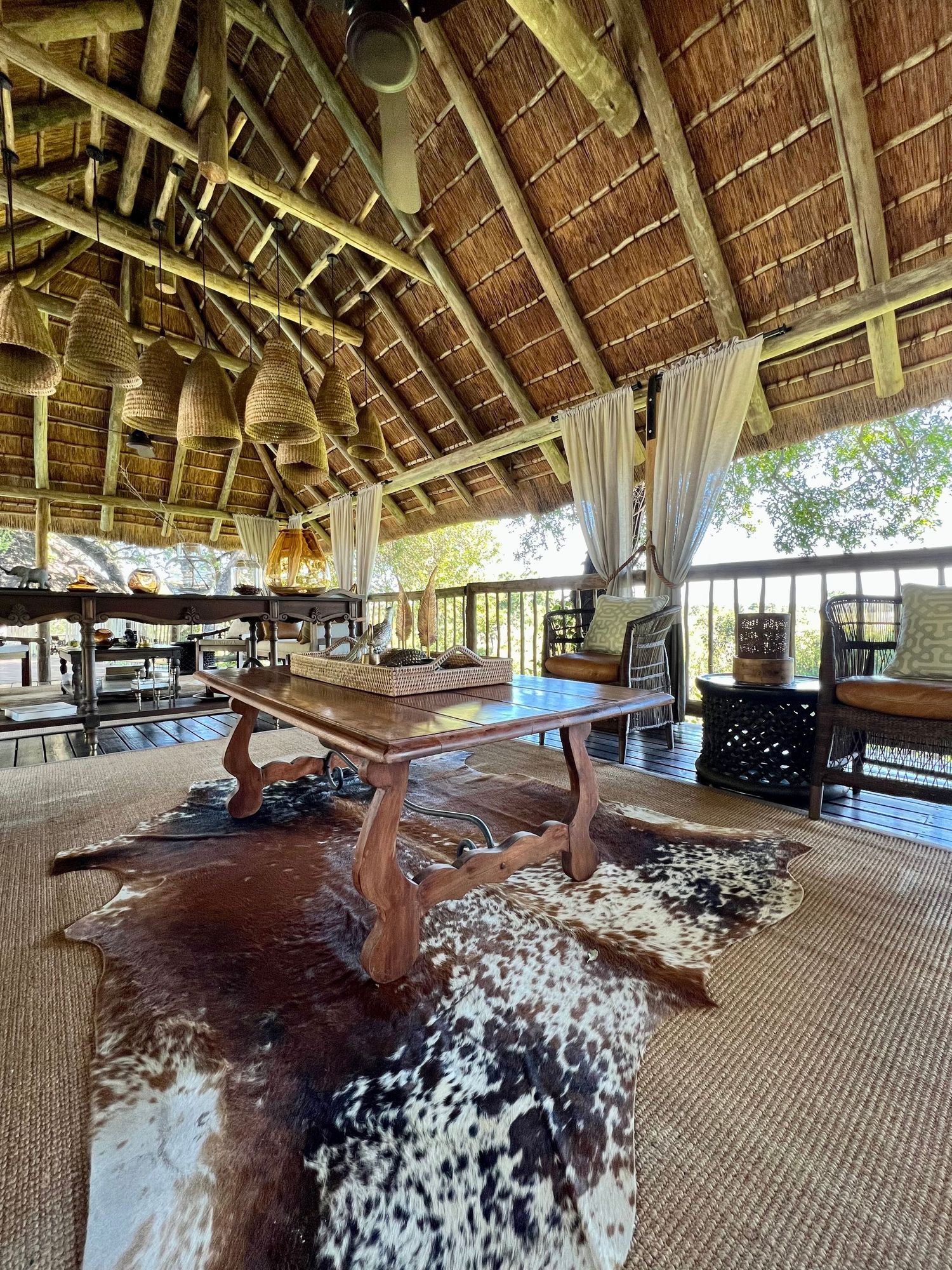 Open-air lodge interior with thatched roof and cowhide rugs on natural woven flooring.