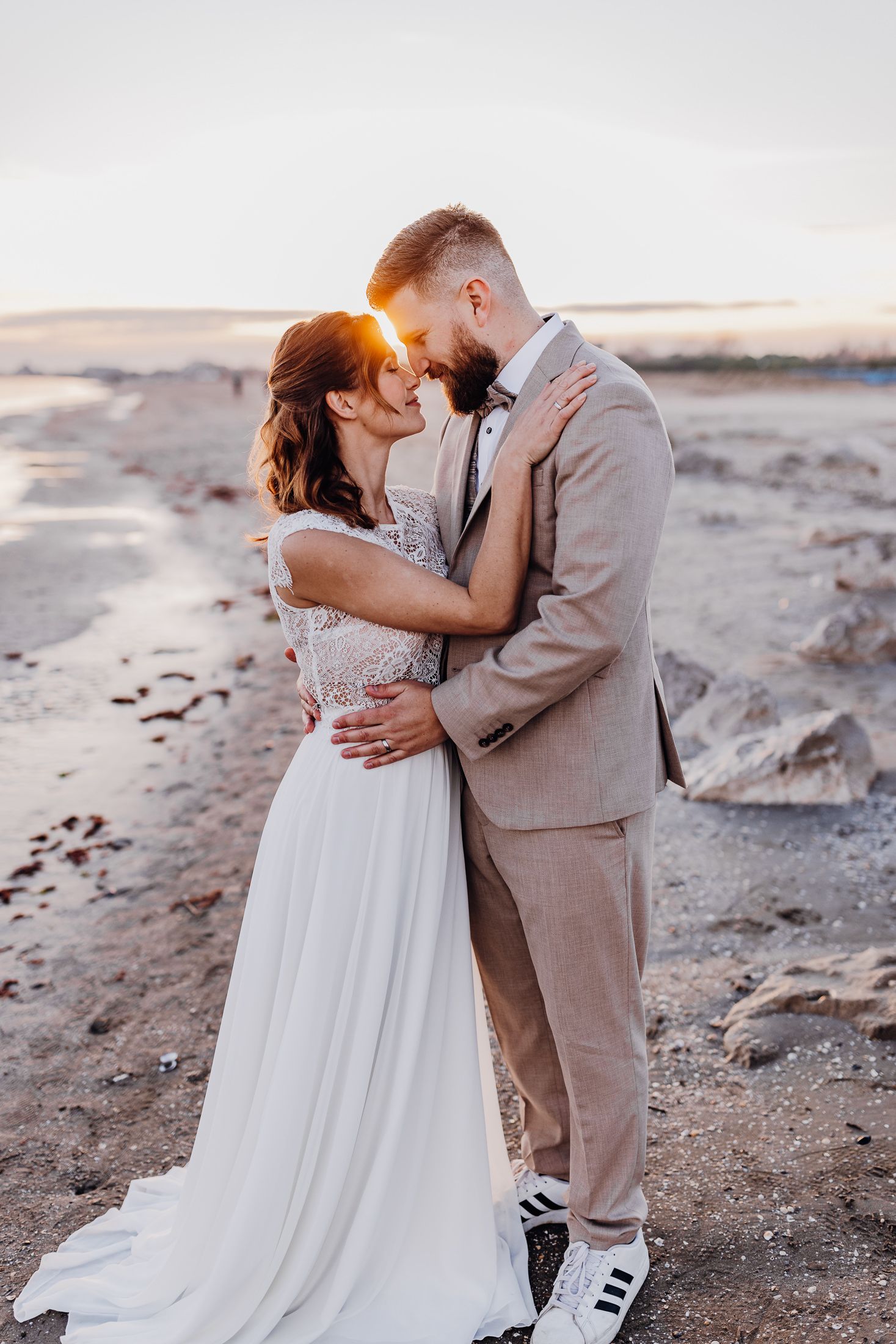 Romantisches Sonnenuntergangshochzeitsfoto mit Paar, das sich auf Strandgelände umarmt.