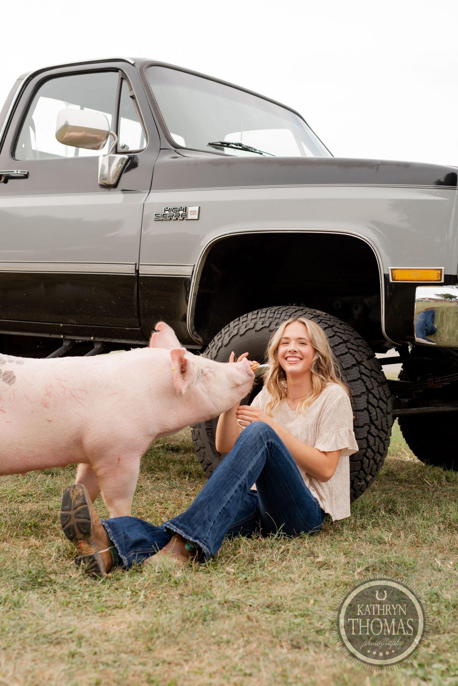 A pink pig interacts with someone sitting by a lifted vintage Chevrolet truck.