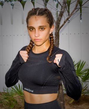 Athletic figure in black crop top with braided hair against white fence.