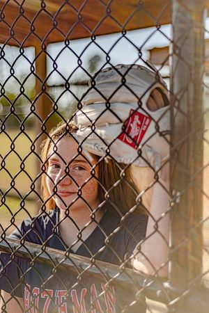 View through chain-link fence of baseball player in dugout.