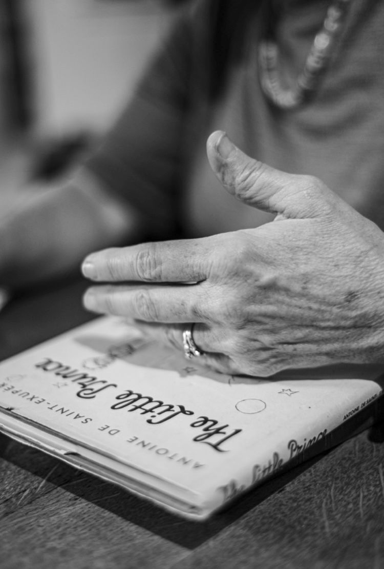 A close-up black and white photo of hands with a ring resting on a book.