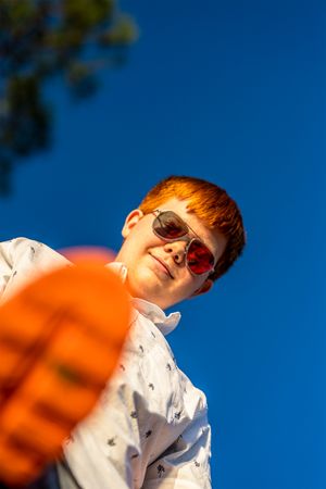 A low angle shot of someone in sunglasses against bright blue sky with orange object in foreground.