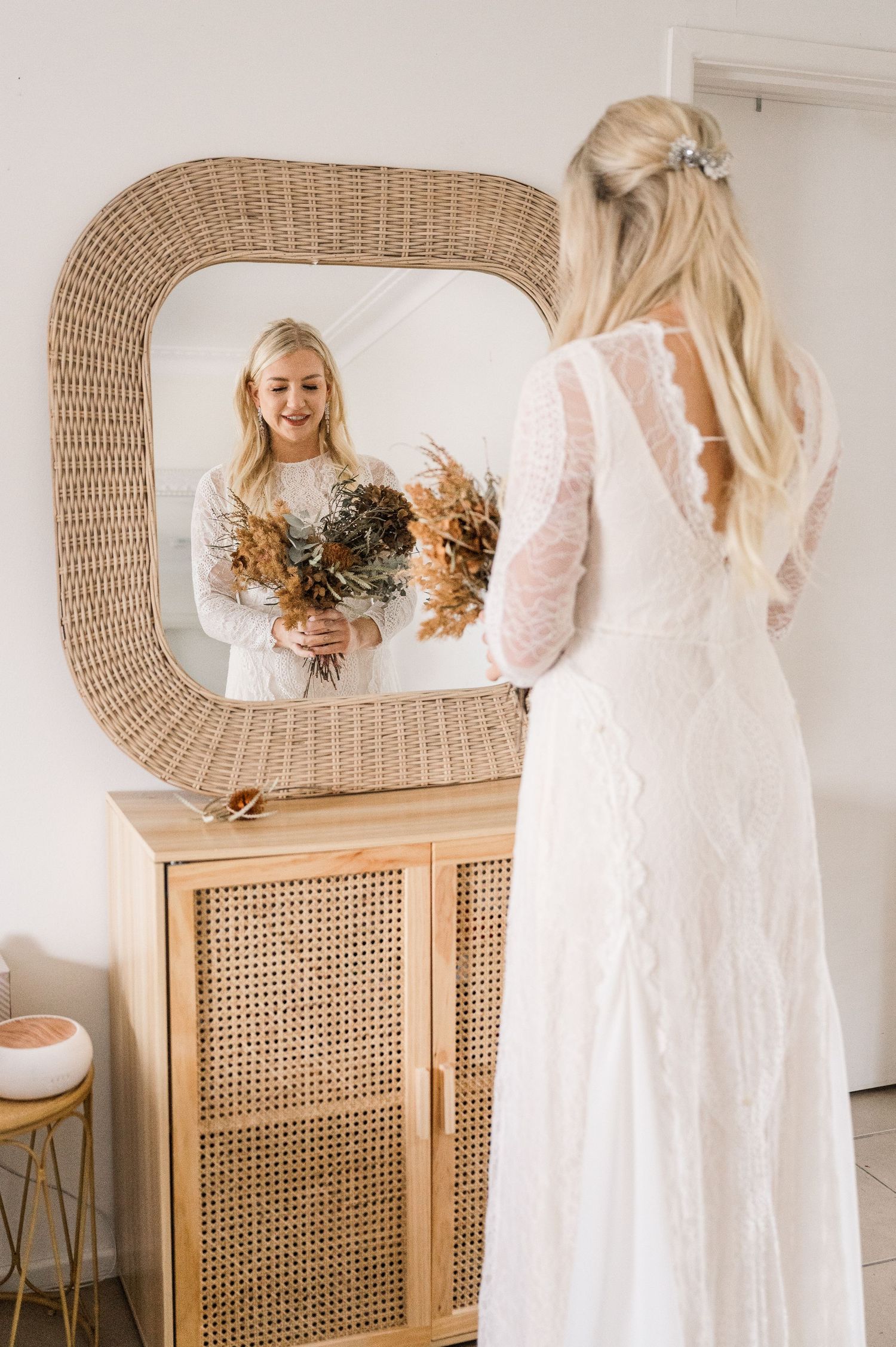 Elegant mirror reflection showing a white lace dress and dried floral bouquet.