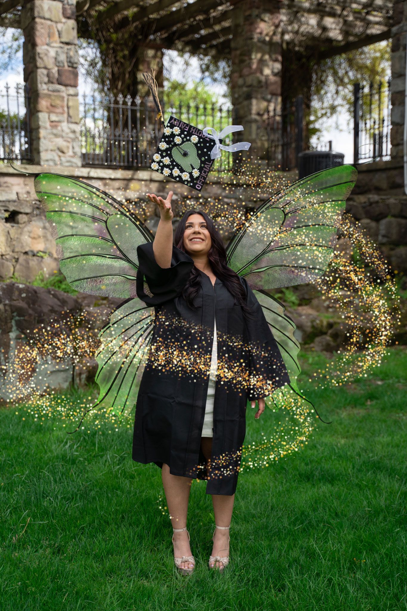 Graduate with digital fairy wings effect posing in front of stone architecture.