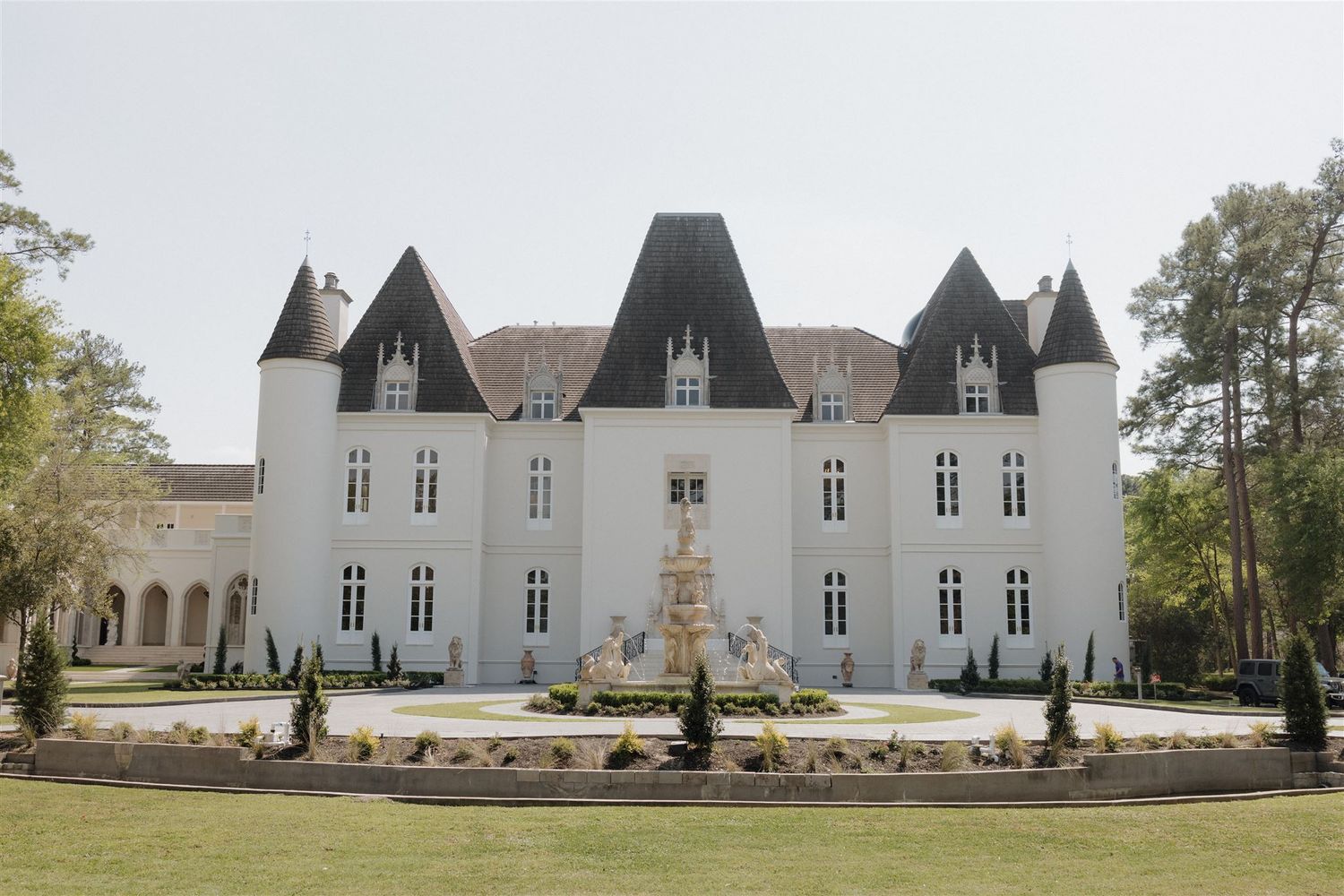 A grand white chateau with multiple spires and a central fountain stands majestically on manicured grounds in France.