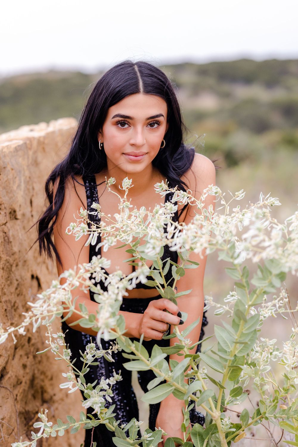 A black outfit styled with delicate white flowers in a natural desert setting.