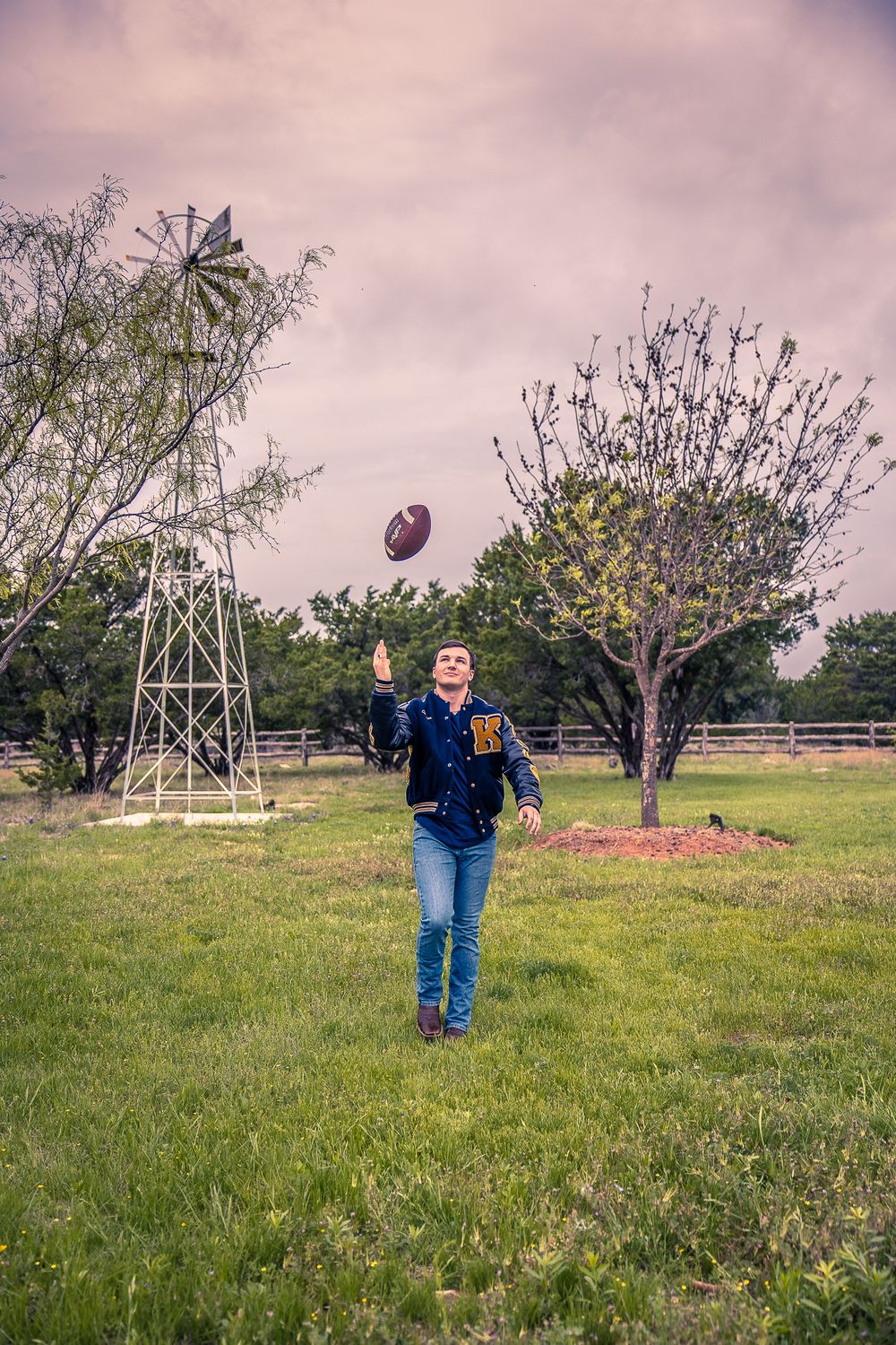 Someone playing with a football in a rustic field with an old windmill in the background.