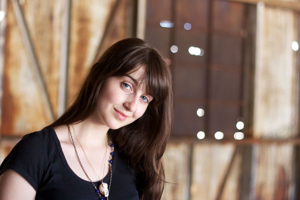 Stylish portrait with long dark hair wearing black top against rustic background.
