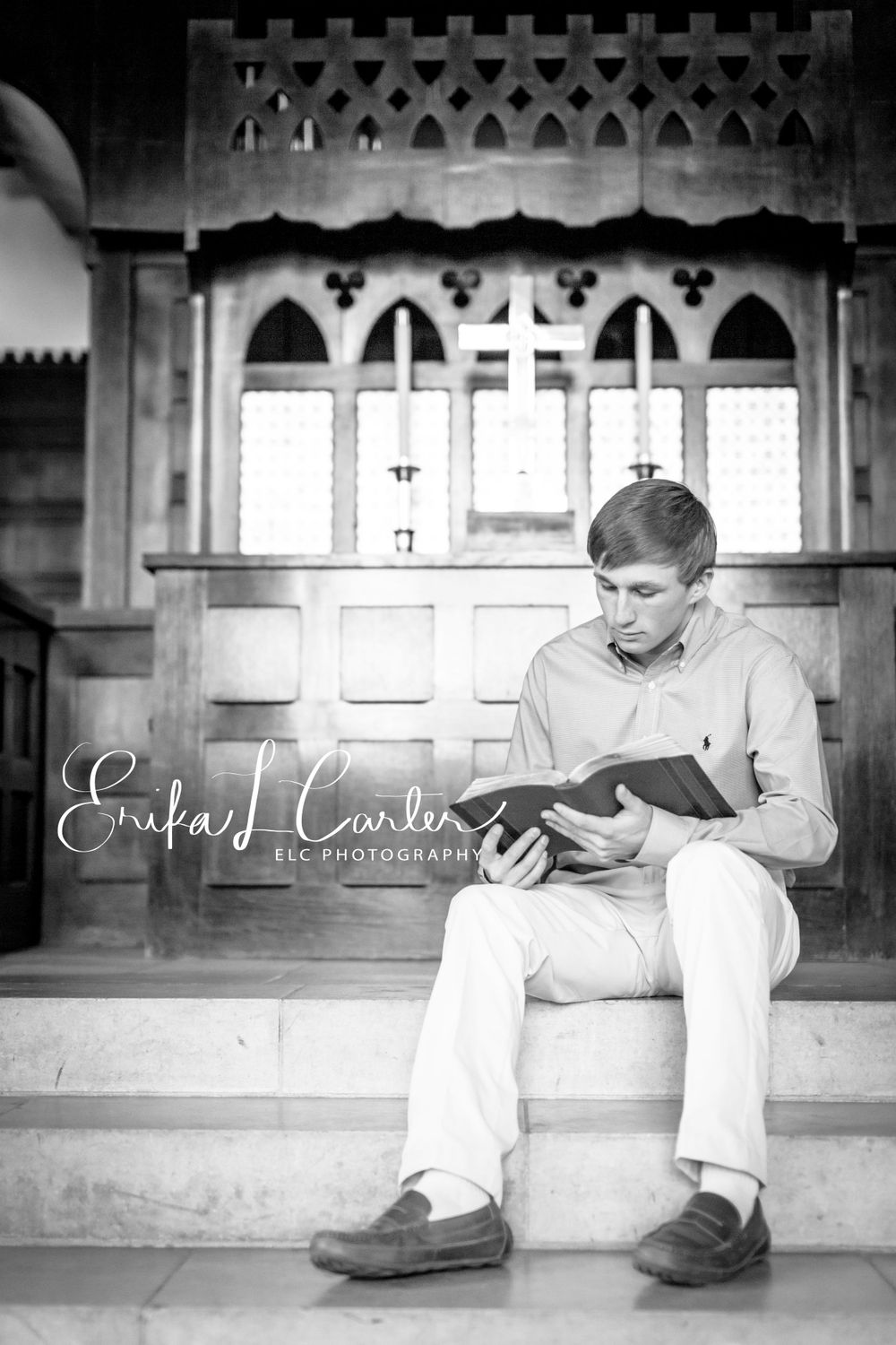 A person reads a book while sitting on stone steps in a black and white architectural setting.