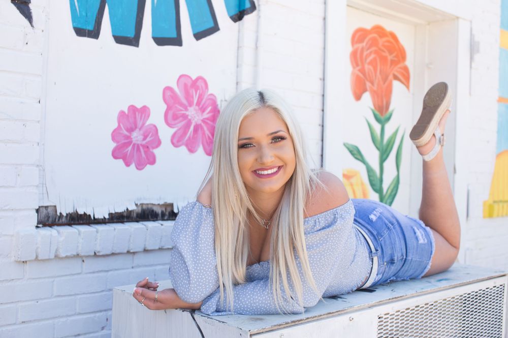 Woman in blue top lounges by colorful floral mural wall.