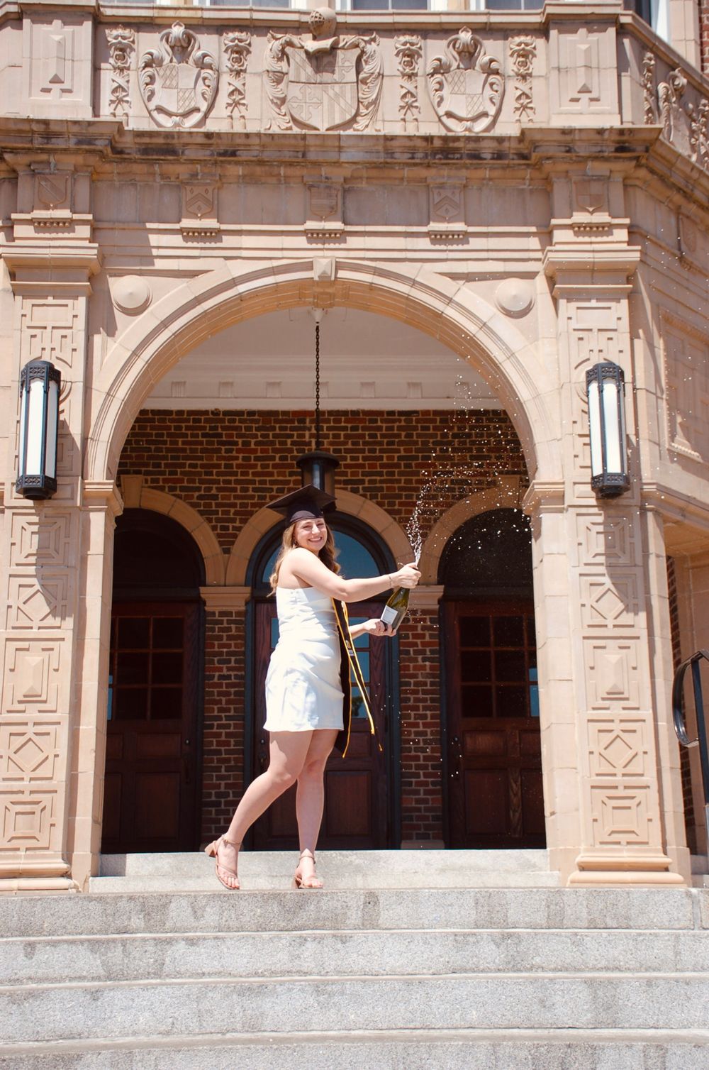 Woman in white dress posing under ornate stone archway of historic building.
