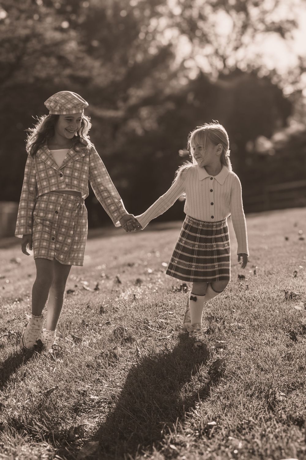 Two girls holding hands while walking on grass in a sepia-toned image.