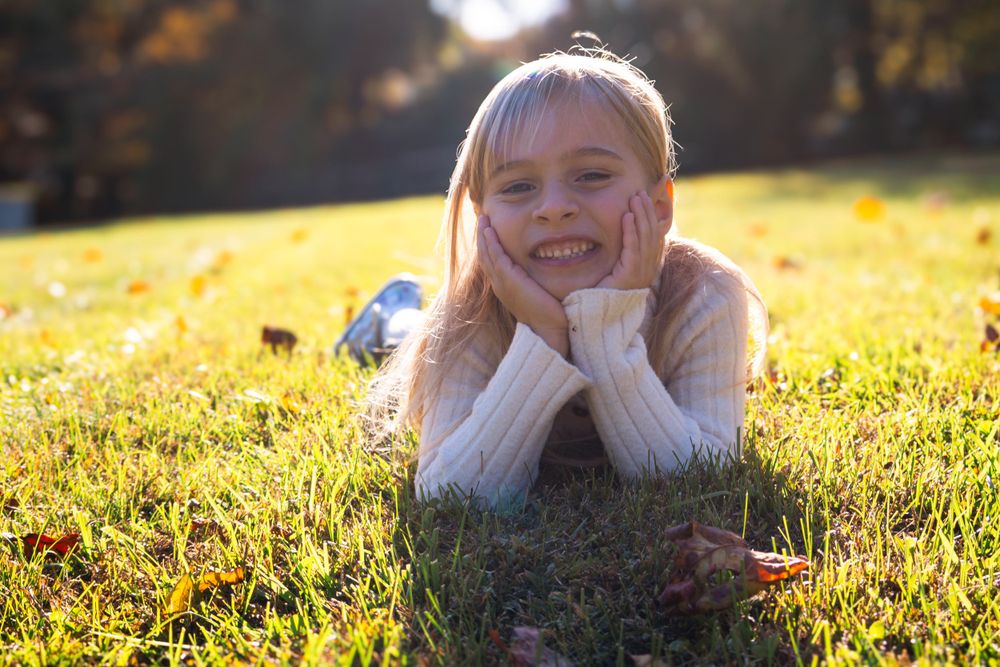 Smiling girl lying on grass with hands under chin in sunny field.