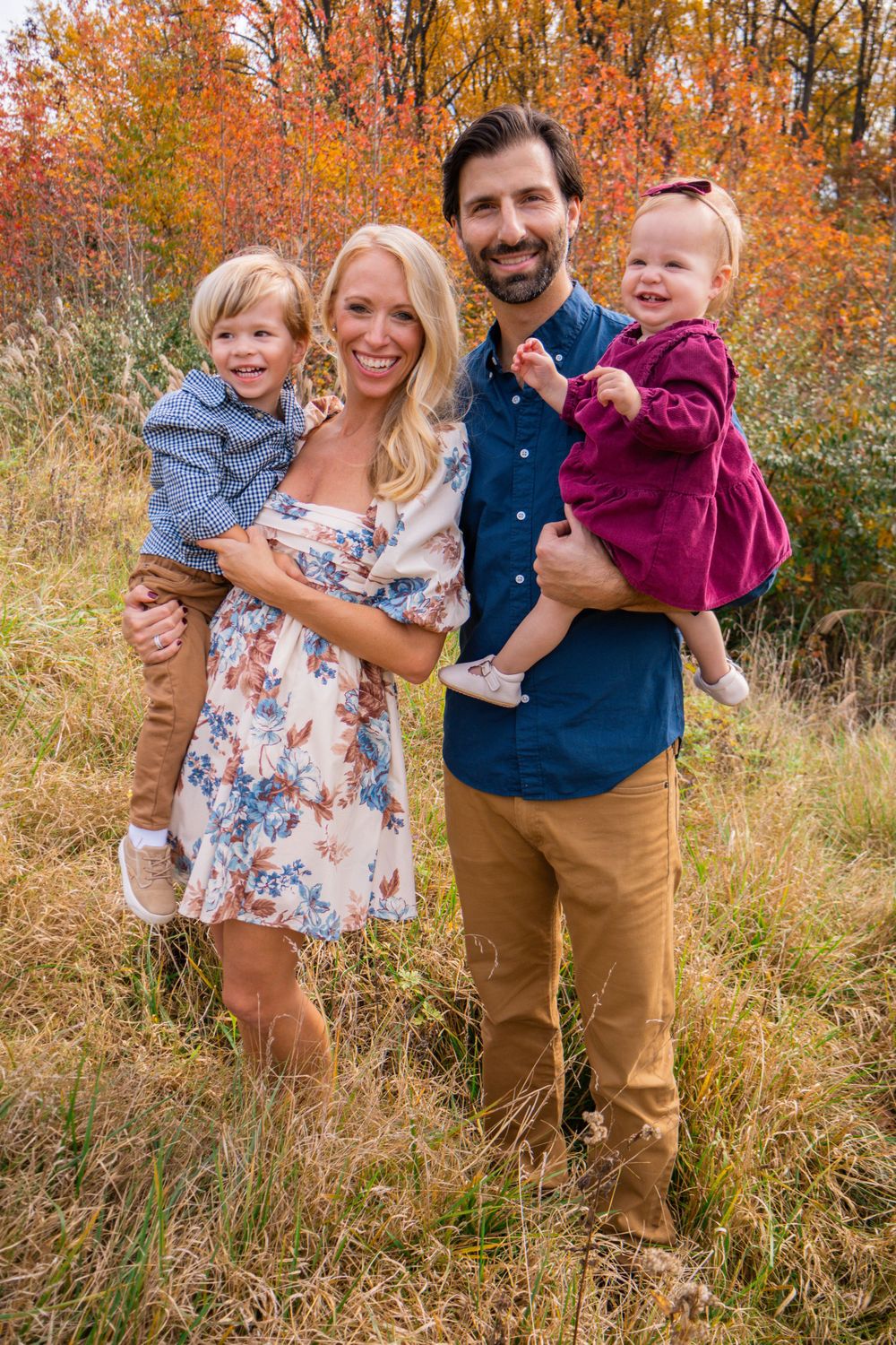 Family of four posing outdoors in front of colorful autumn foliage.