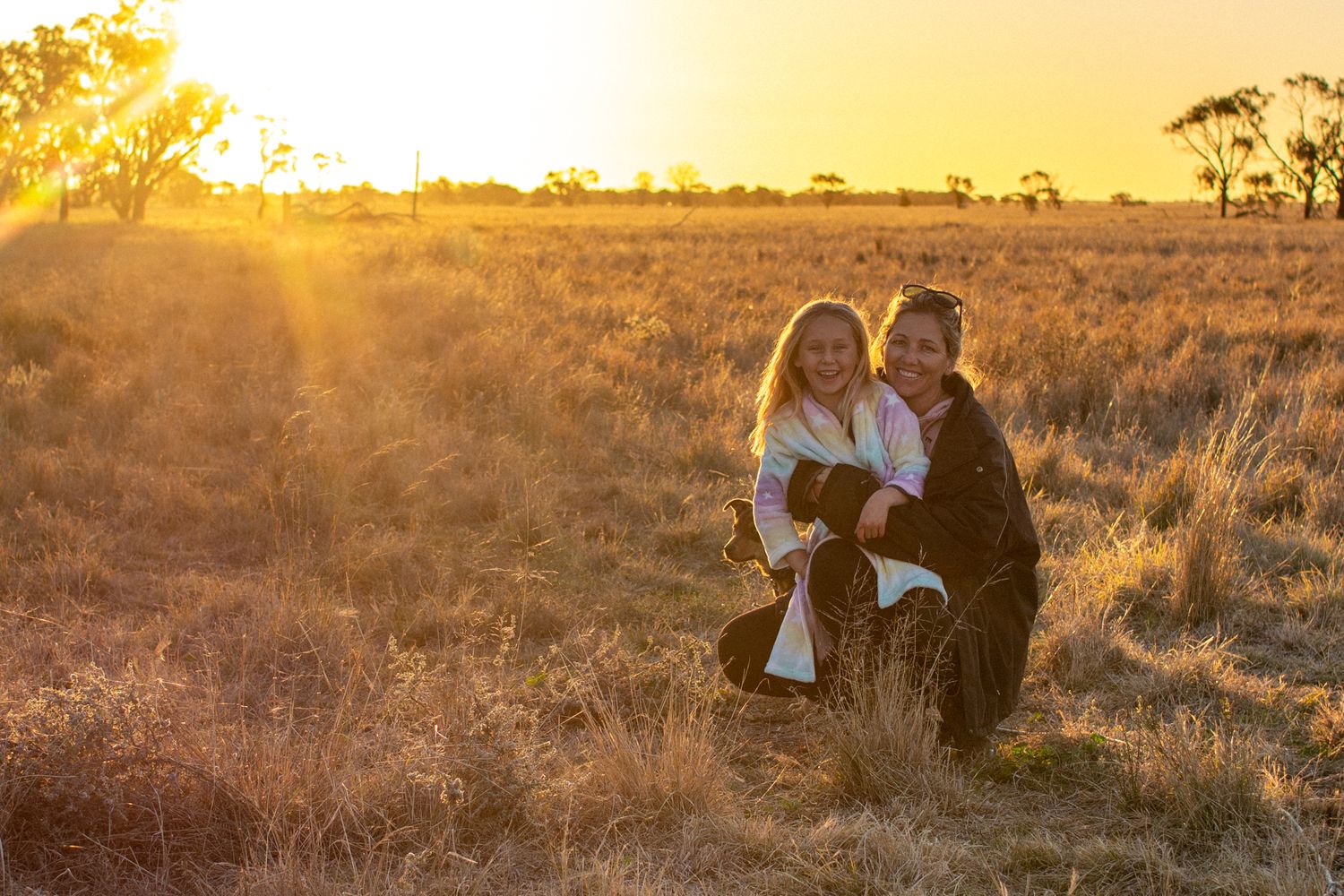 Mum and daughter in the winter sunset, sitting in a paddock.