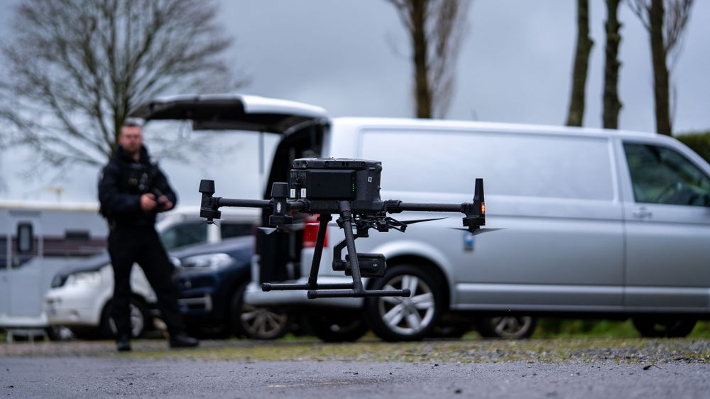 Drone setup with equipment near a silver van outdoors.
