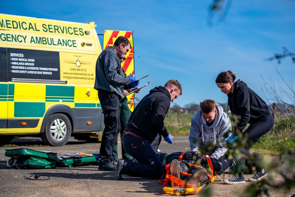Emergency medical personnel attend to a situation next to an ambulance vehicle on a sunny day.