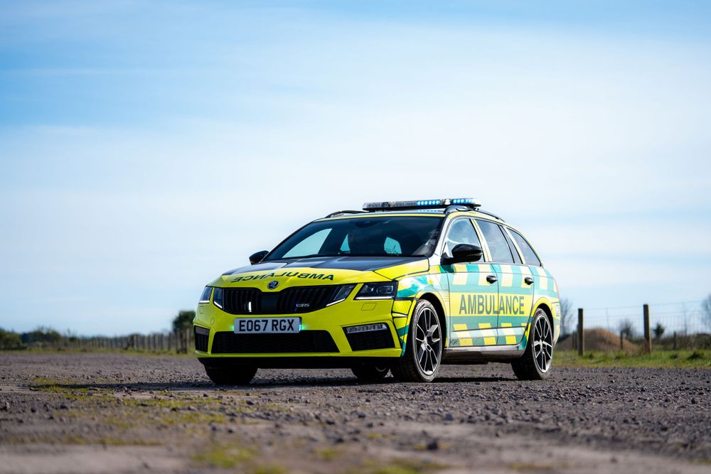 Yellow and green emergency response vehicle parked on a dirt road against blue sky.