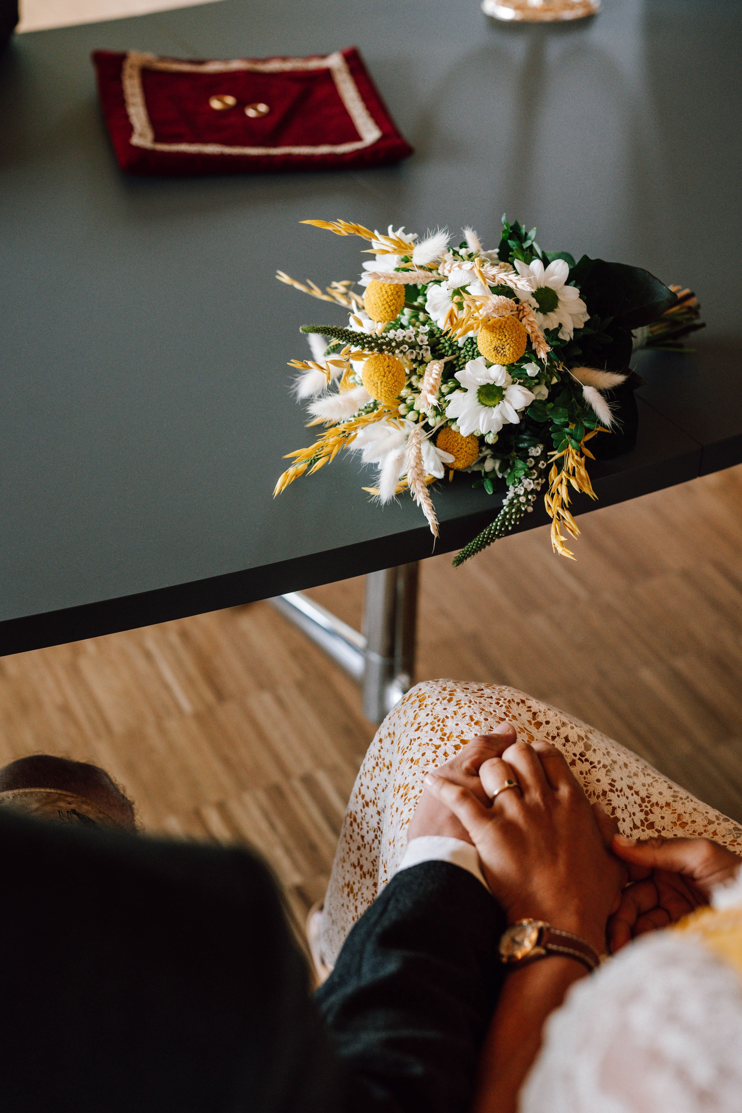 A close-up shot of hands and flowers on a dark table during a wedding ceremony.