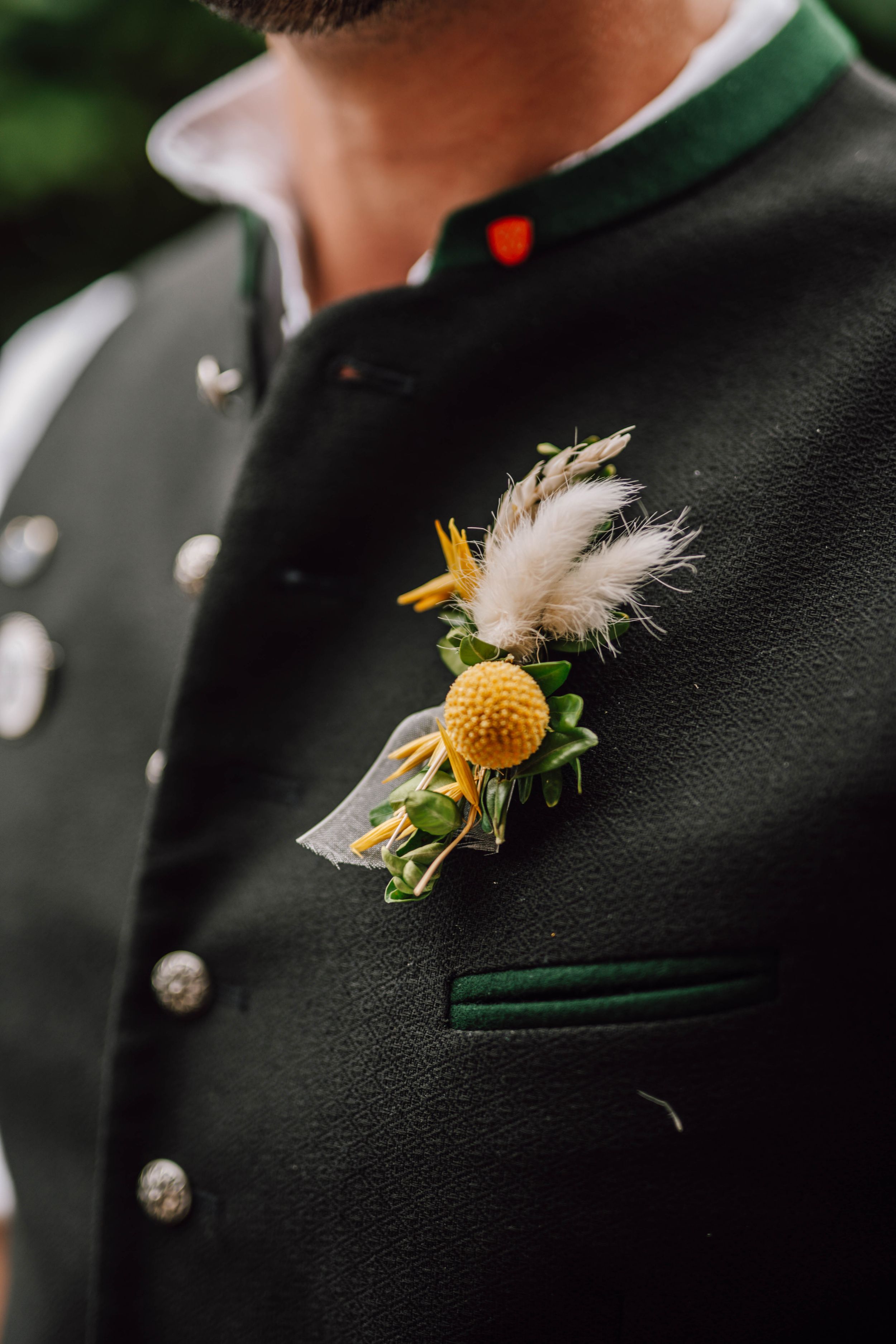 Traditional Bavarian wedding boutonnieres with yellow flowers and white feathers on dark jackets.