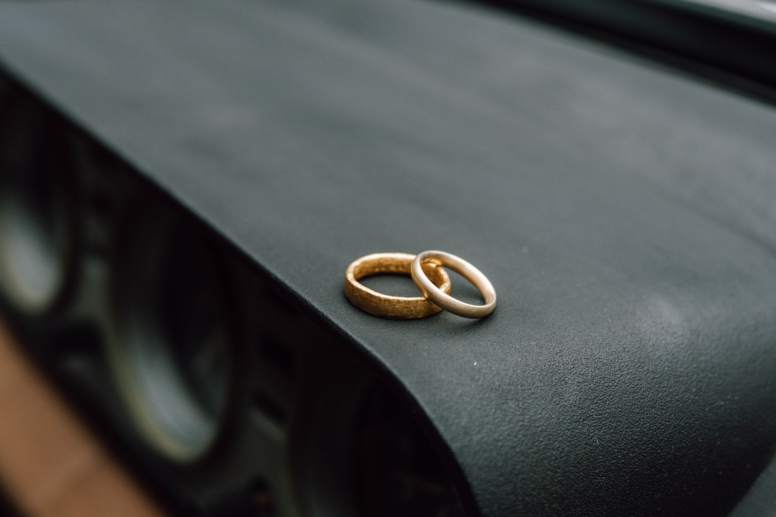 Two gold wedding rings resting on a dark surface in soft lighting.
