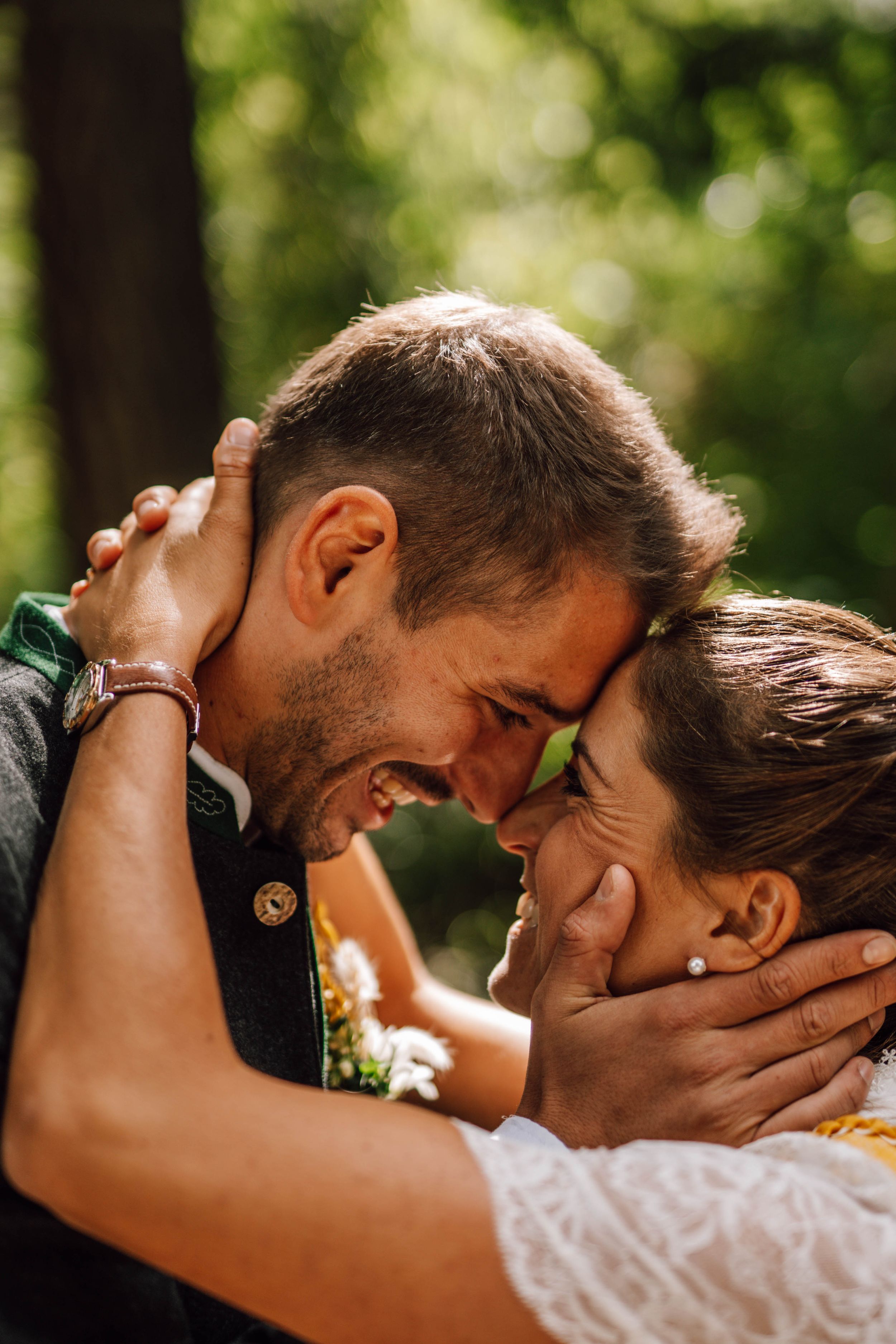 A couple shares joyful laughter and embraces in a sunlit outdoor setting.
