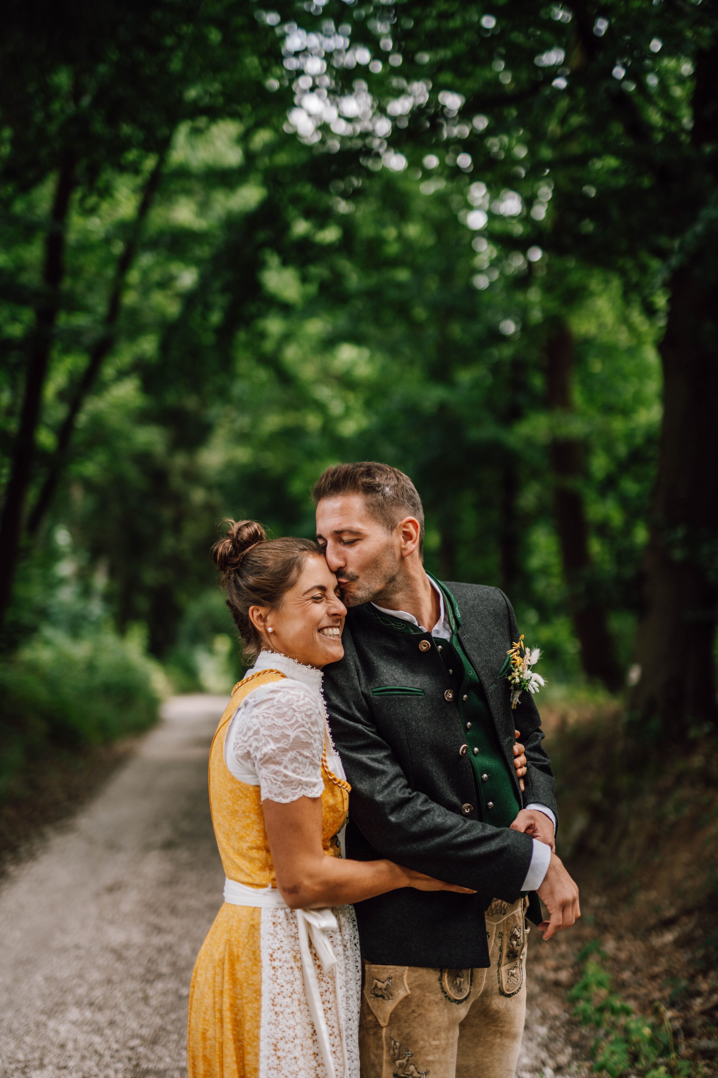 A couple in Bavarian wedding attire sharing a romantic moment on a gravel path.