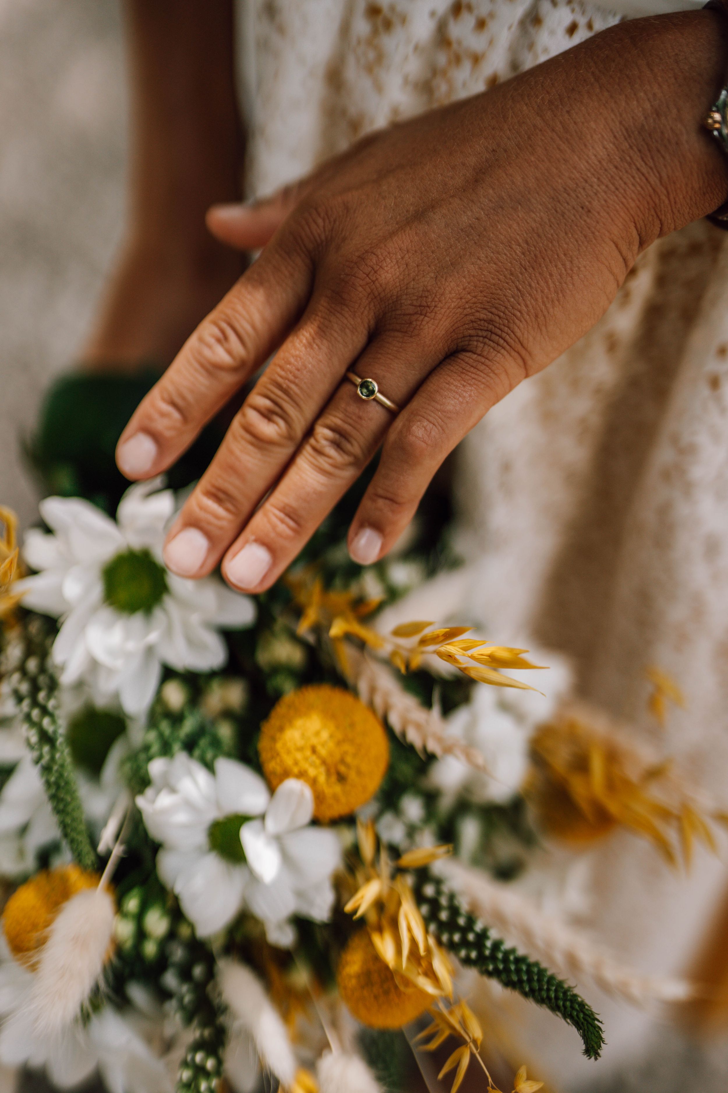 Close-up of hands arranging white and yellow flowers with greenery for a wedding bouquet.