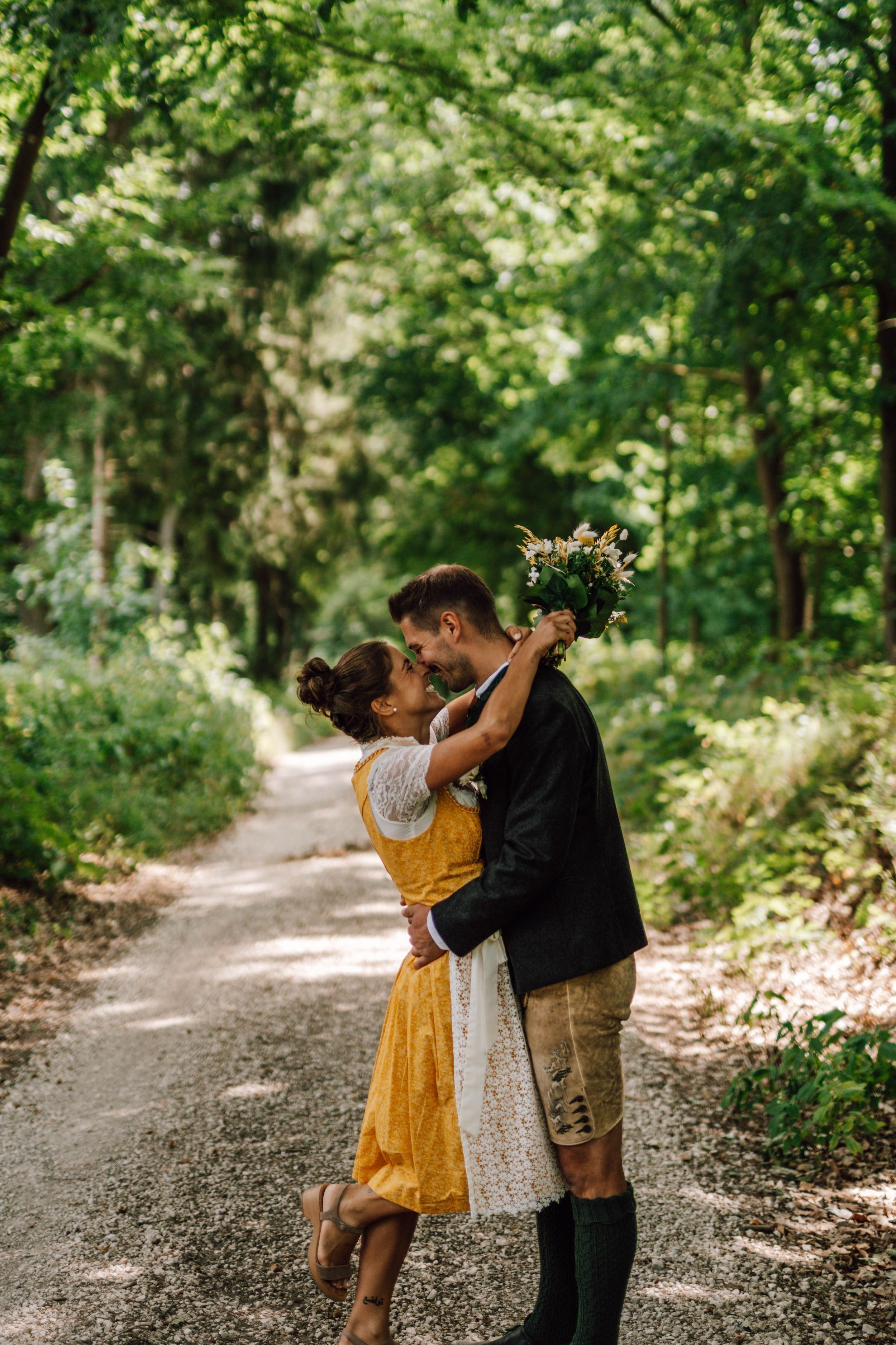 A couple in traditional dress dancing and laughing together on a forest path.