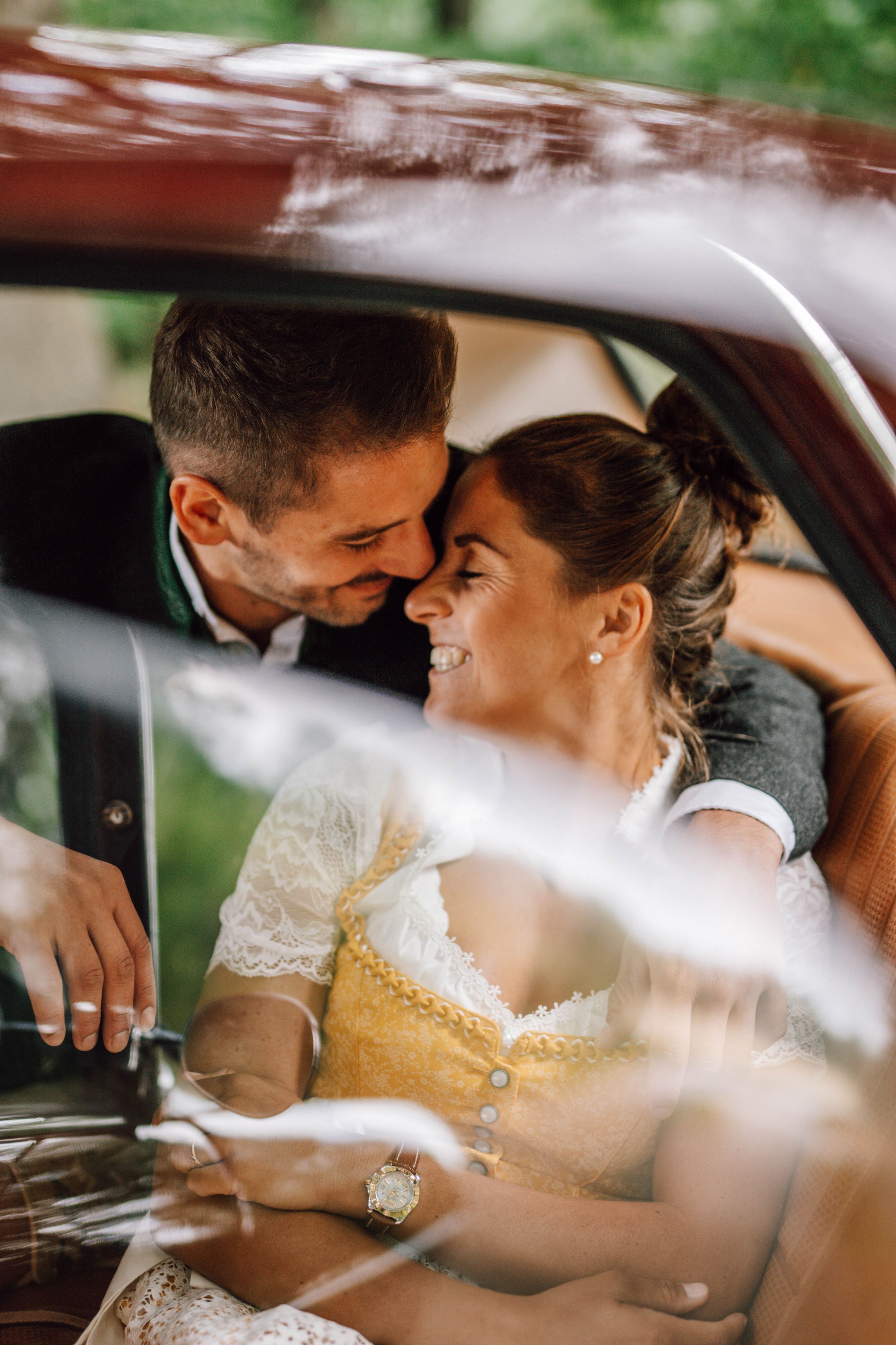 Intimate wedding moment captured through car window with natural outdoor backdrop.